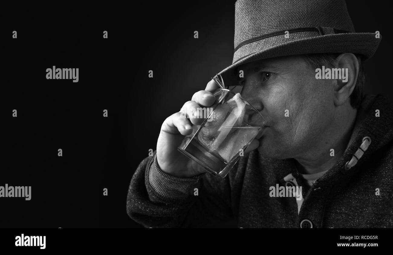 Middle-aged man in a hat drinking an alcoholic cocktail with lemon. Black and white. Copy space. Stock Photo