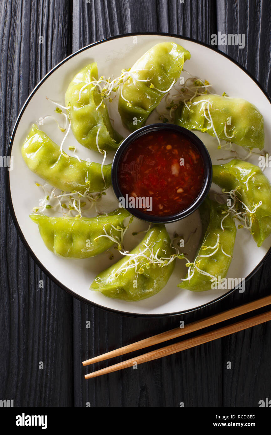 Fresh green gyoza dumplings with matcha are served with spicy chili sauce and microgreen close-up on a plate on the table. Vertical top view from abov Stock Photo