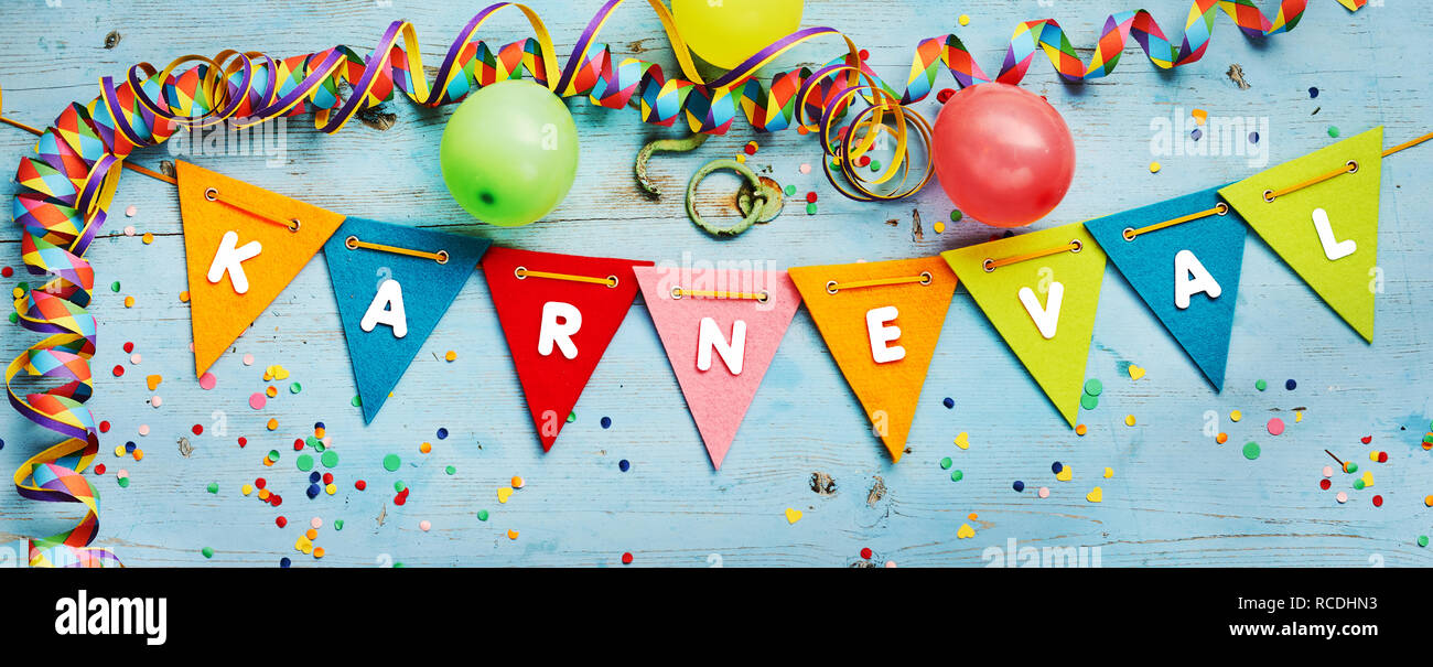 Karneval - Carnival - themed festive party banner background with triangular rainbow colored bunting and streamers forming a border on blue wood with  Stock Photo