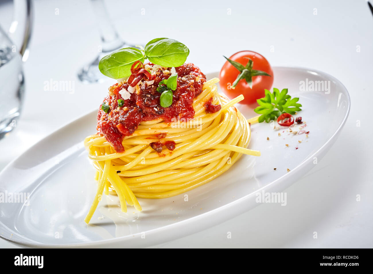 Spaghetti Bolognaise With Tomato Topping Sprinkled With Parmesan Cheese And Spices And Garnished With Basil Served With A Fresh Tomato On A Tilted Whi Stock Photo Alamy