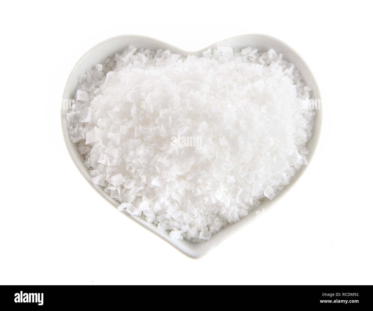 Heart shaped bowl of Flor de Sal, a Portuguese salt derived from the evaporation of sea water, viewed from above isolated on white Stock Photo