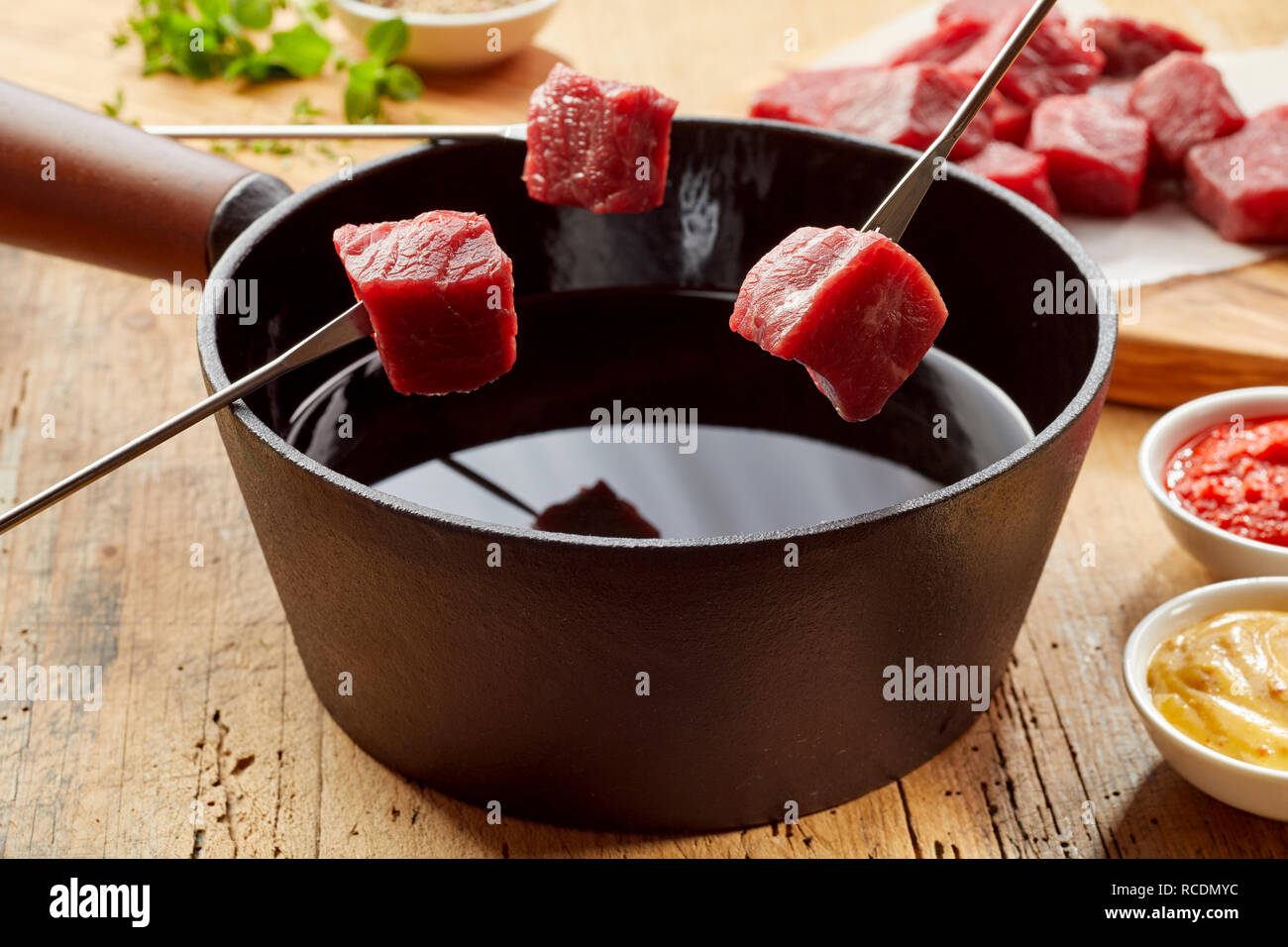 Raw fresh beef on fondue forks ready for dipping into the hot oil in a close up view with sides