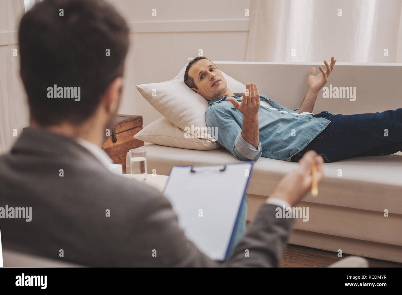 Stressed man lying on beige sofa explaining his problems to therapist Stock Photo