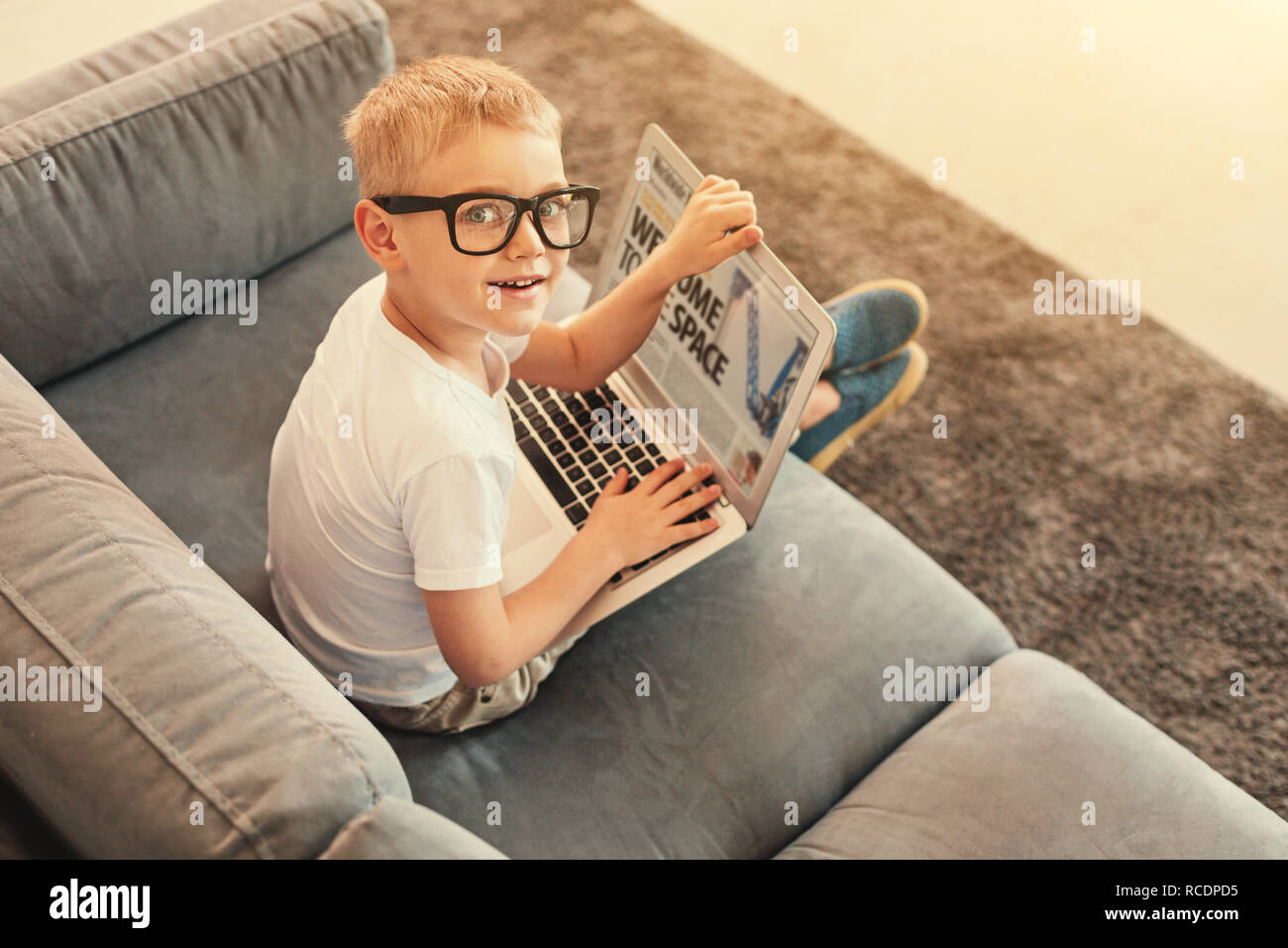Informative reading. The top view of an adorable little boy sitting on the sofa and holding a laptop while reading an article on it Stock Photo