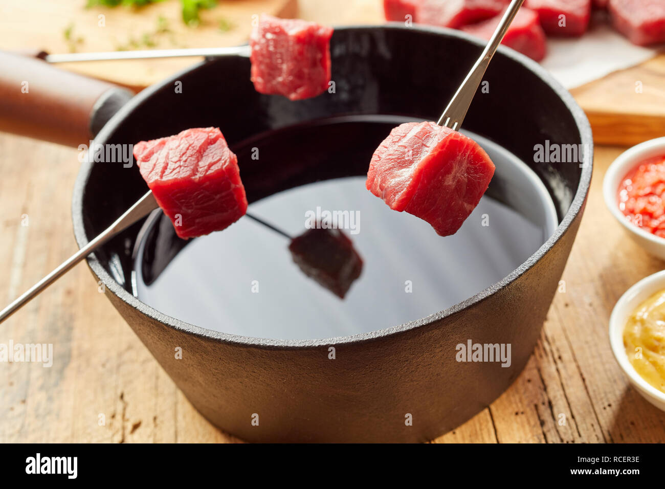 Traditional meat fondue with diced raw beef held ready on forks over the pot of hot oil in a