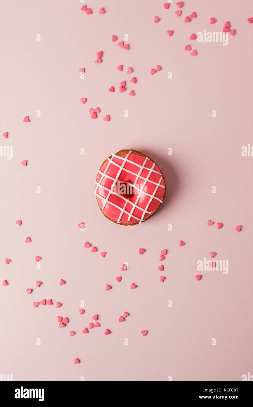 One pink live coral donut and heart shaped sprinkles on pink background, monochrome seet unhealthy food concept, flat lay, top view, copy space Stock Photo