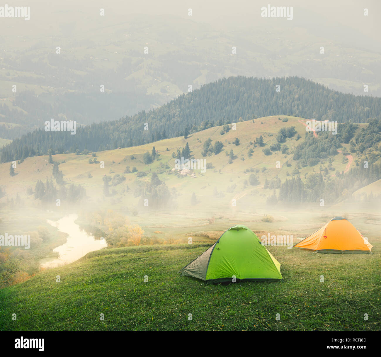 Green and orange tents on plain in mountains on foggy morning Stock Photo