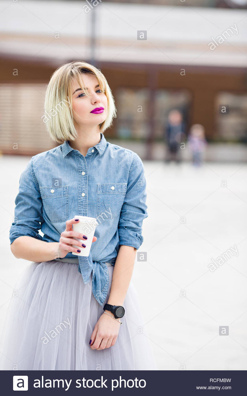 A Portrait Of A Standing Dreamy Blonde Girl With Bright Pink Lips Hoding A Cup Of Cofee Wearing Denim Shirt Grey Tulle Skirt And Black Watch Stock Photo Alamy