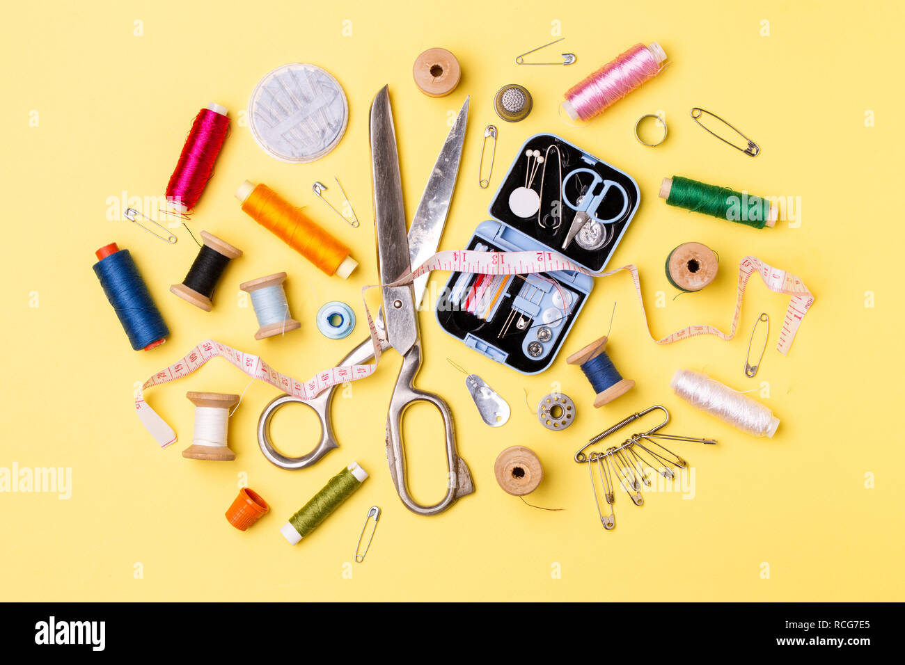 Composition with threads and sewing accessories - scissors, centimeter, pins on yellow background. Stock Photo