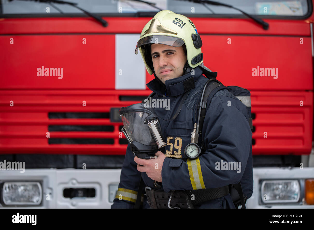 Photo of man fireman with mask in hands near fire truck Stock Photo