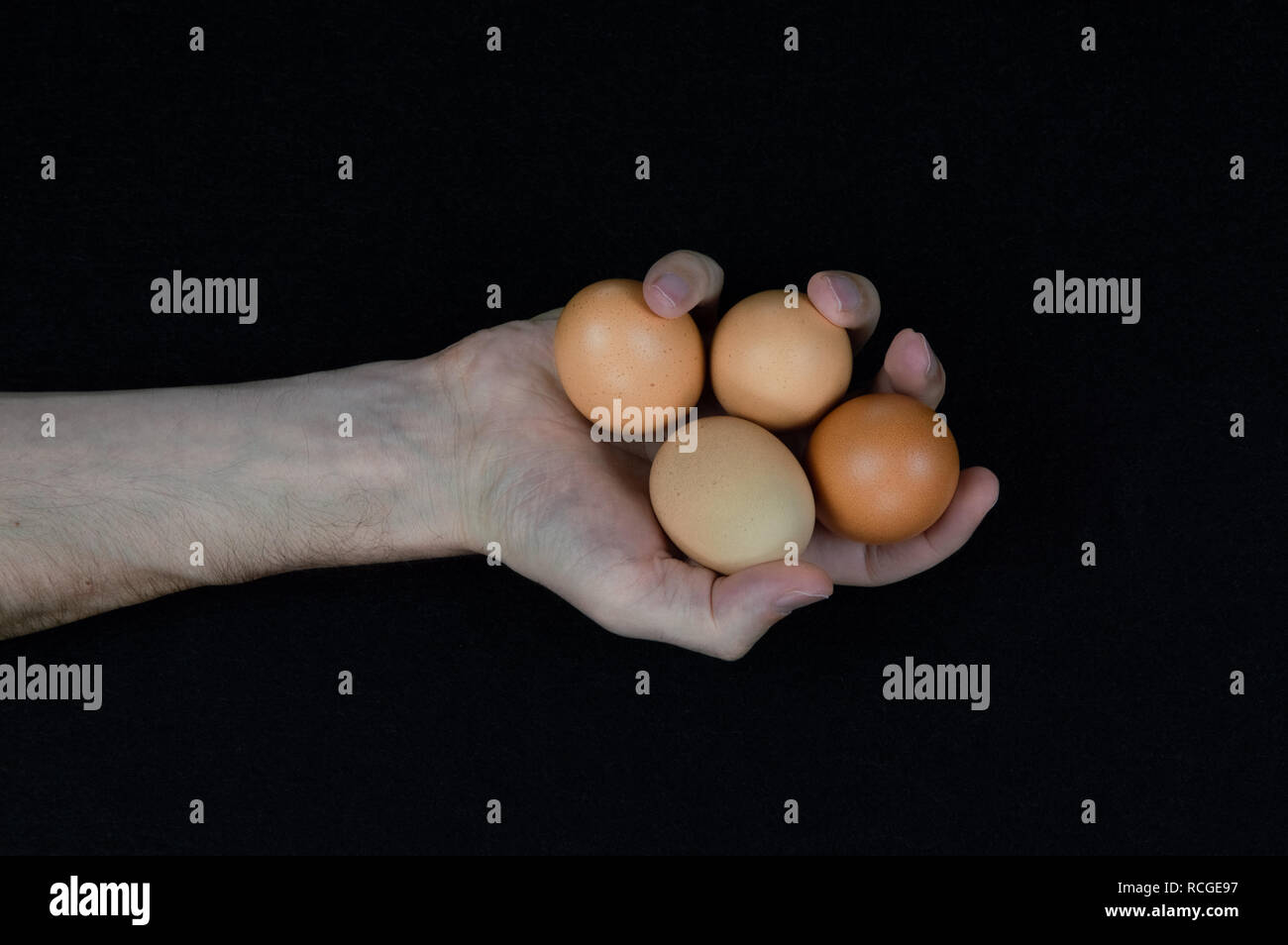 Man holding four brown eggs in his hand on a black felt background Stock Photo