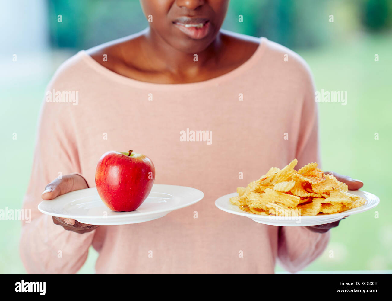 Ethnic girl undecided whether to have crisps or an apple to eat Stock Photo