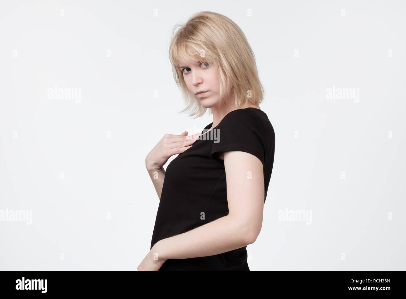 Headshot of young woman pointing on herself verbally defending herself, having perplexed and puzzled expression on her face, saying Who me. Stock Photo