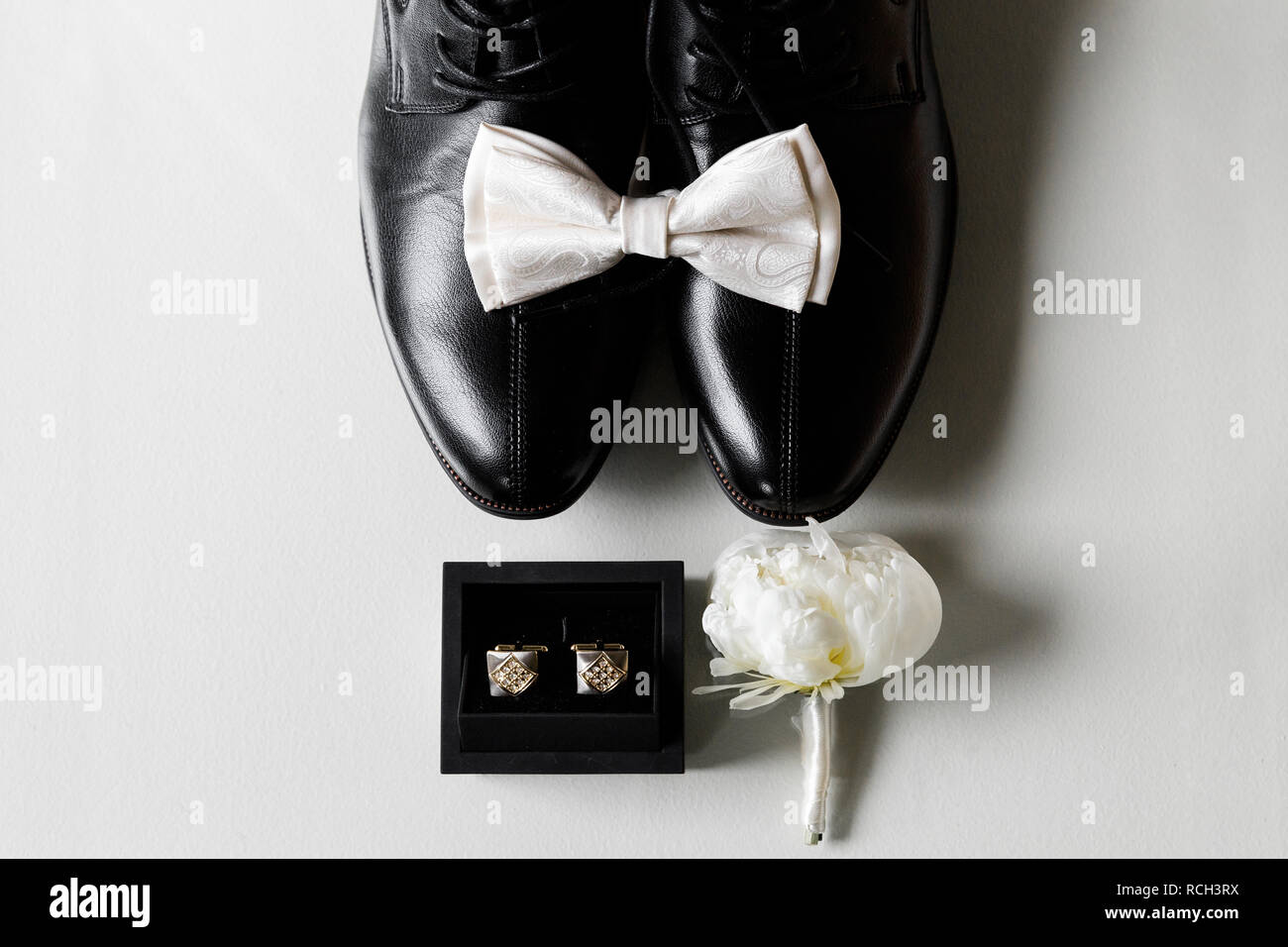 Photo of a white bow tie on black shoes, next to a box with cufflinks and boutonniere. Close-up on a white background. Stock Photo