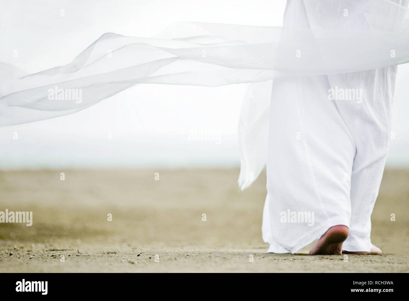 Photo of a man walking in a white robe on the sand. A picture from the back, a person is visible to the waist, clothes are fluttering in the wind Stock Photo