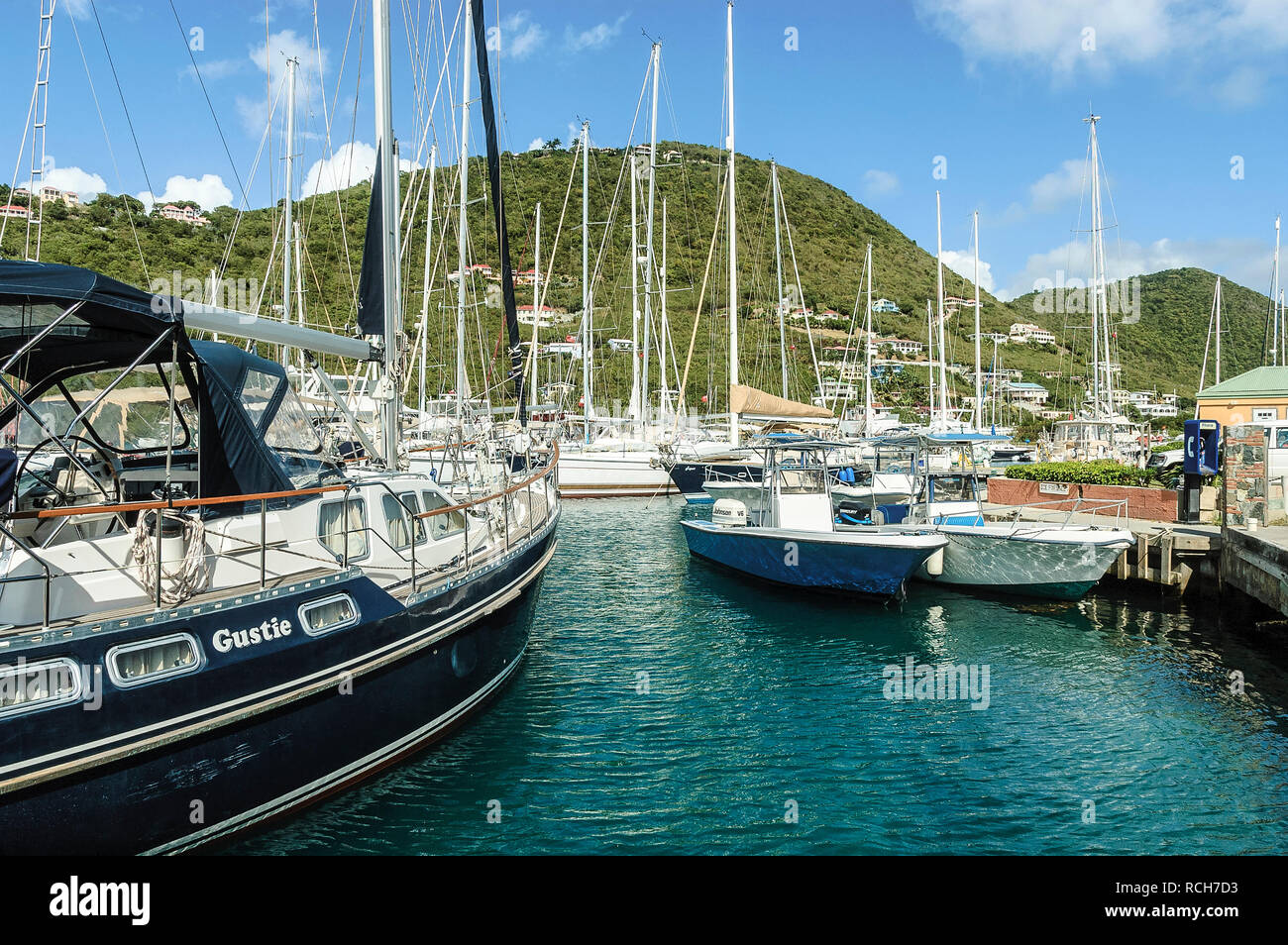 A forest of masts and rigging from boats moored at Soper's Hole Wharf intersperse with the view of green verdant hills opposite Stock Photo