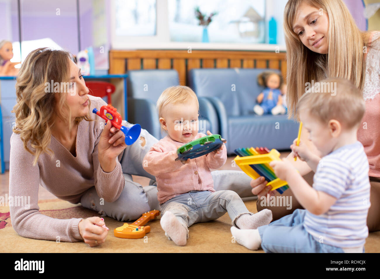 Nursery babies playing musical toys with teacher and assistant. Early