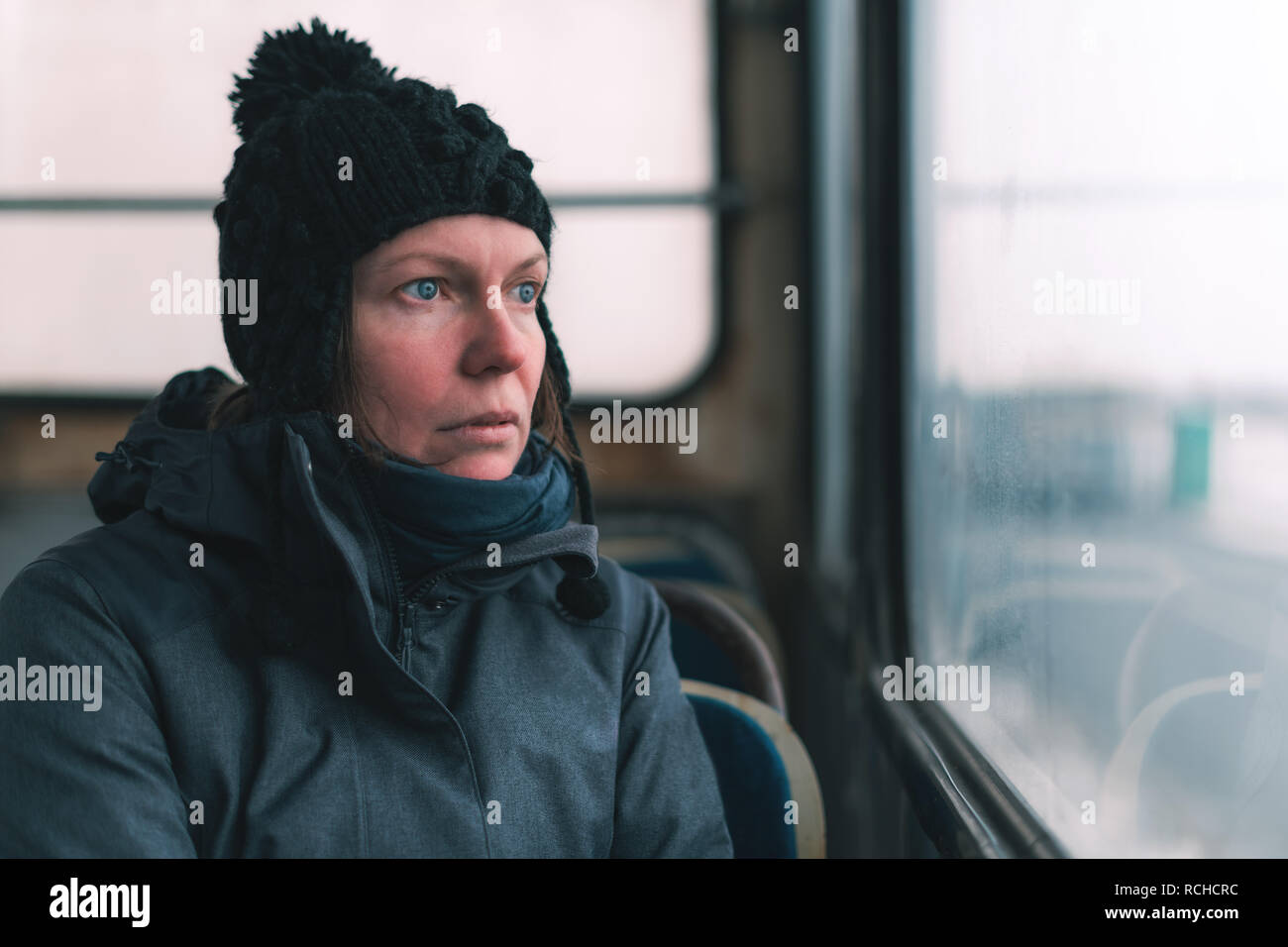 Sad woman on the bus looking through window at the street on cold winter day Stock Photo
