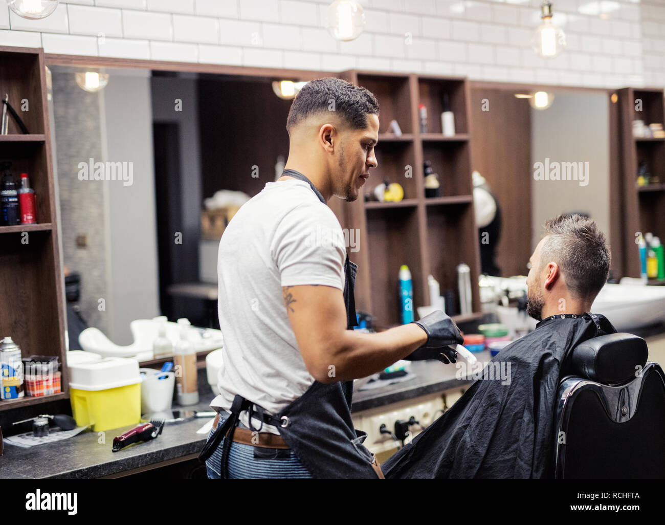 Rear view of man client visiting haidresser and hairstylist in barber shop. Stock Photo