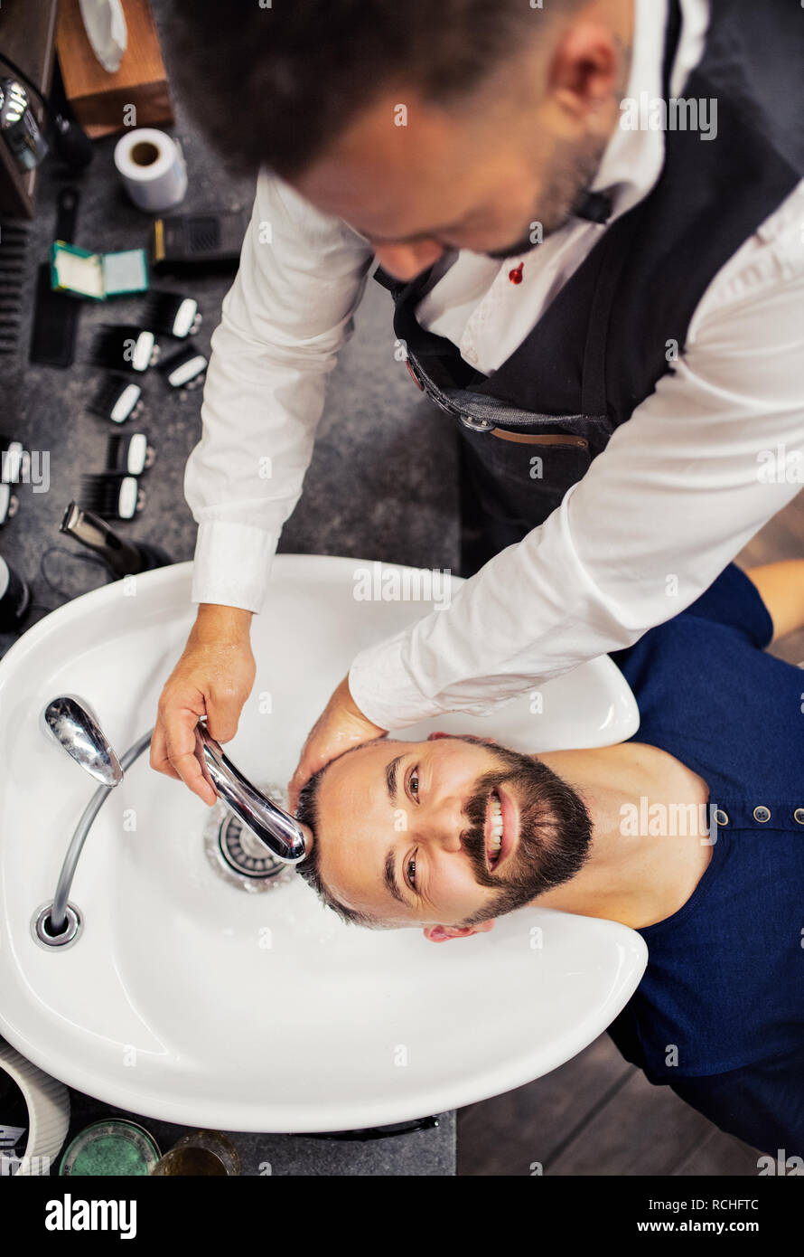 A top view of hipster man client visiting haidresser and hairstylist in barber shop. Stock Photo