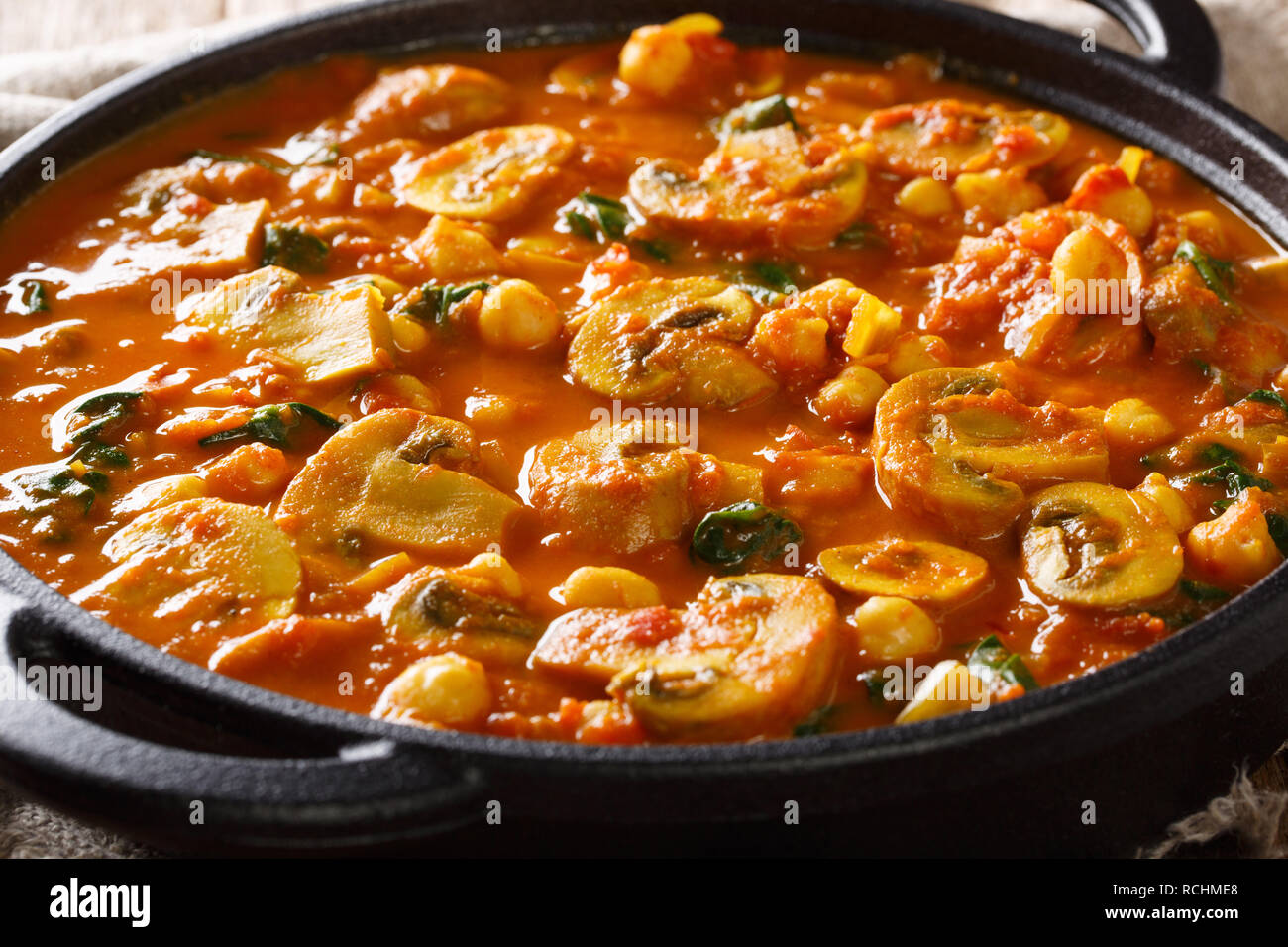 Hot Asian mushroom curry with spinach and chickpeas close-up in a frying pan. horizontal Stock Photo