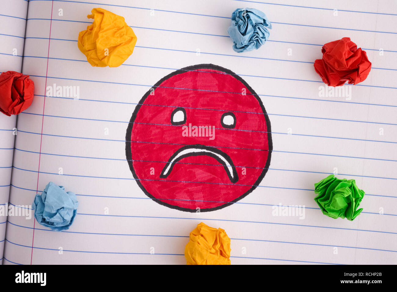Sad face with colorful crumpled paper balls on notebook sheet. Close up. Stock Photo