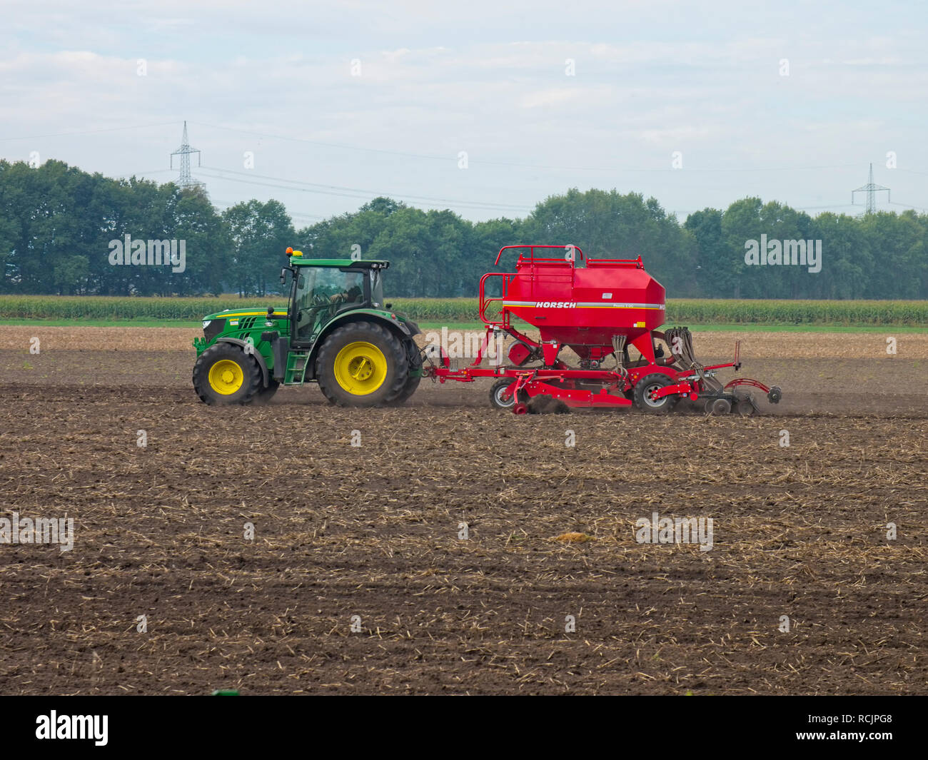 Farmer on his tractor combined with a sawing machine sawing gras on  a field  near Mechtersen, Niedersachsen, Germany. Stock Photo