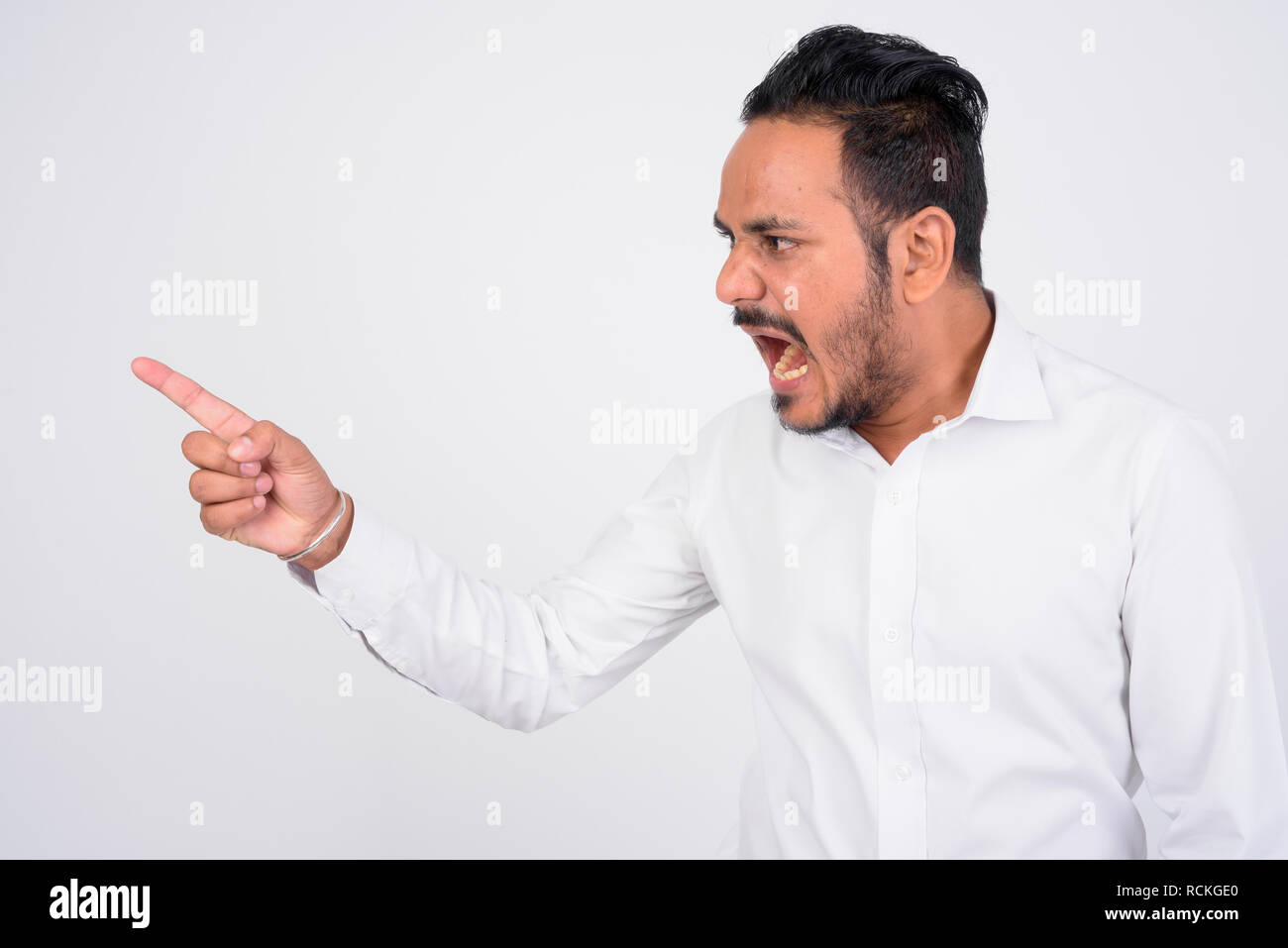 Studio shot of angry bearded Indian businessman shouting and pointing finger Stock Photo