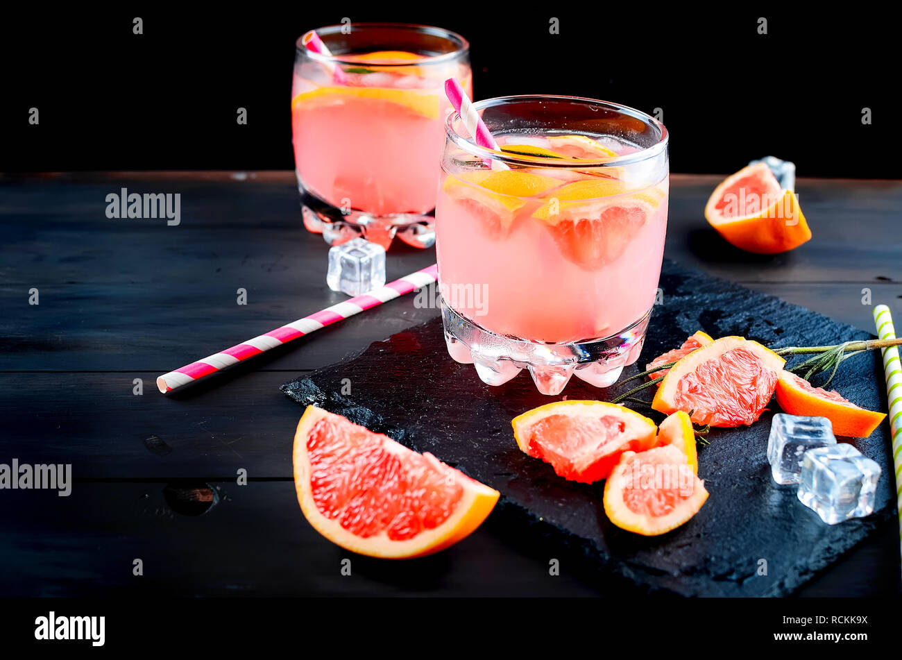 grapefruit juice or cocktail in glasses and pieces of grapefruit, ice cubes, straws on a dark background Stock Photo