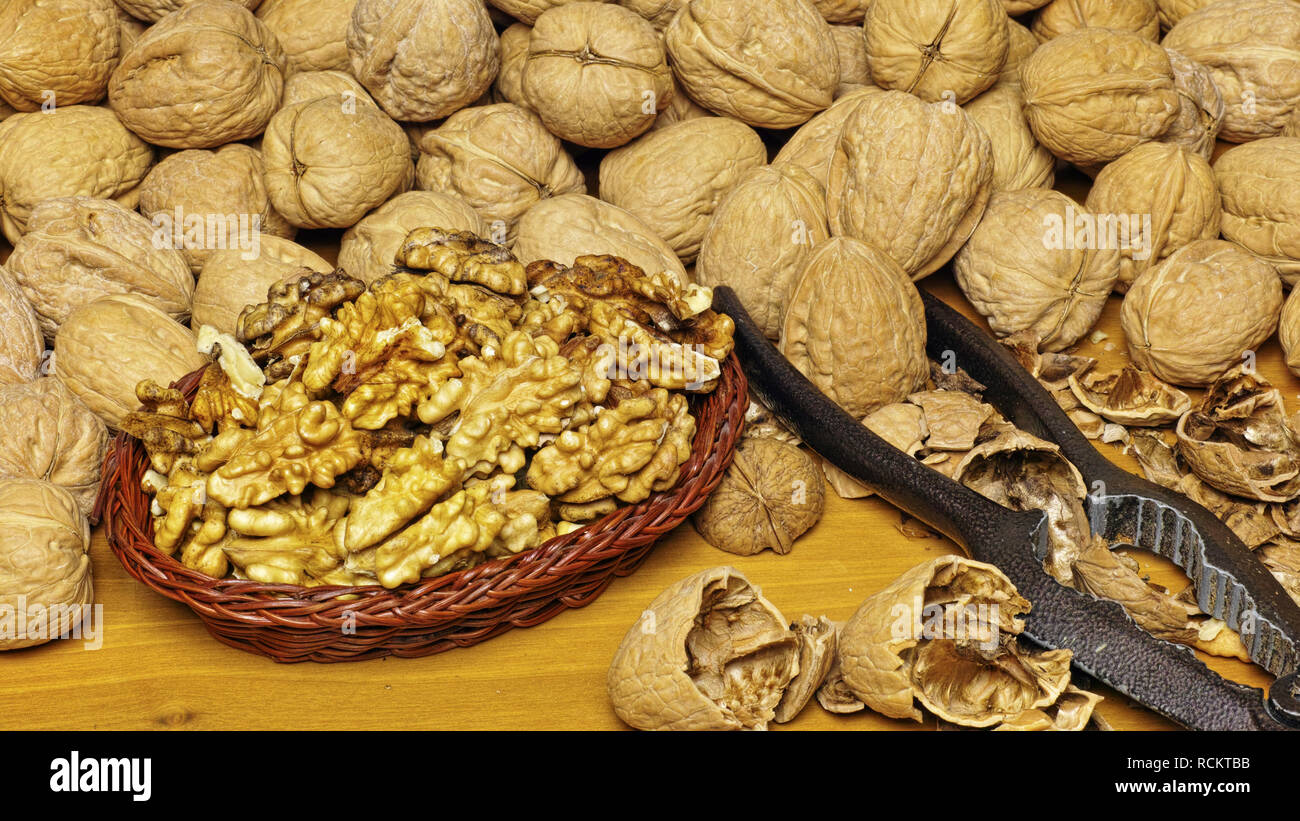 little basket full of kernels, a nutcracker with some broken shells and many nuts around it Stock Photo