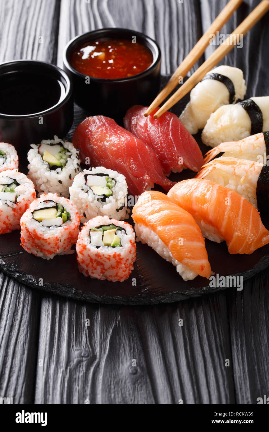 Japanese sushi food served on blackboard plate with two sauces. Sushi roll with prawn, avocado, salmon, tuna, sesame close-up. Vertical Stock Photo