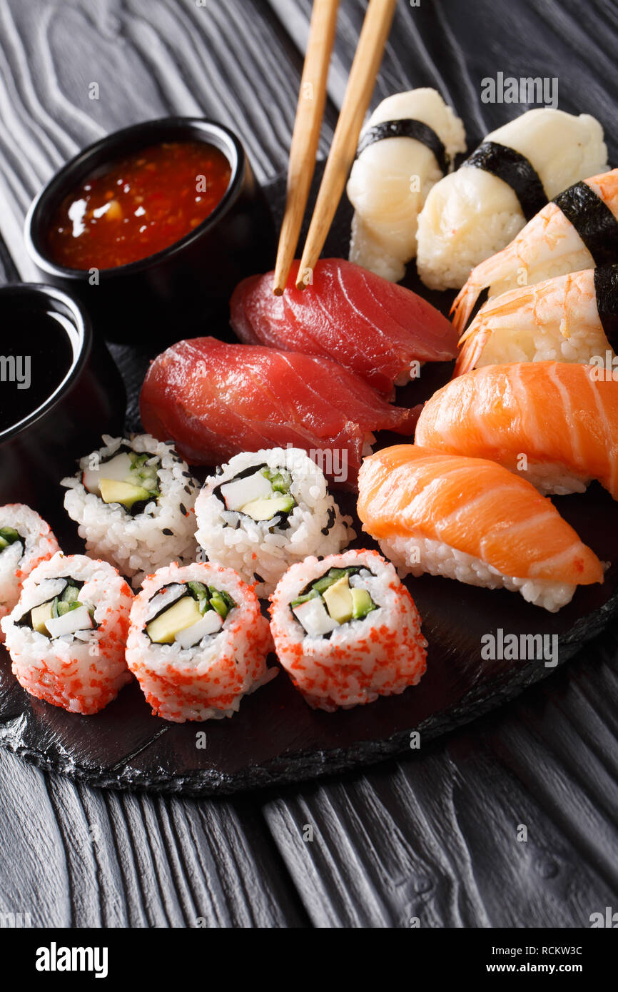 Japanese sushi food. Maki ands rolls with tuna, salmon, shrimp, crab and avocado with two sauces close-up on a slate plate. Vertical Stock Photo