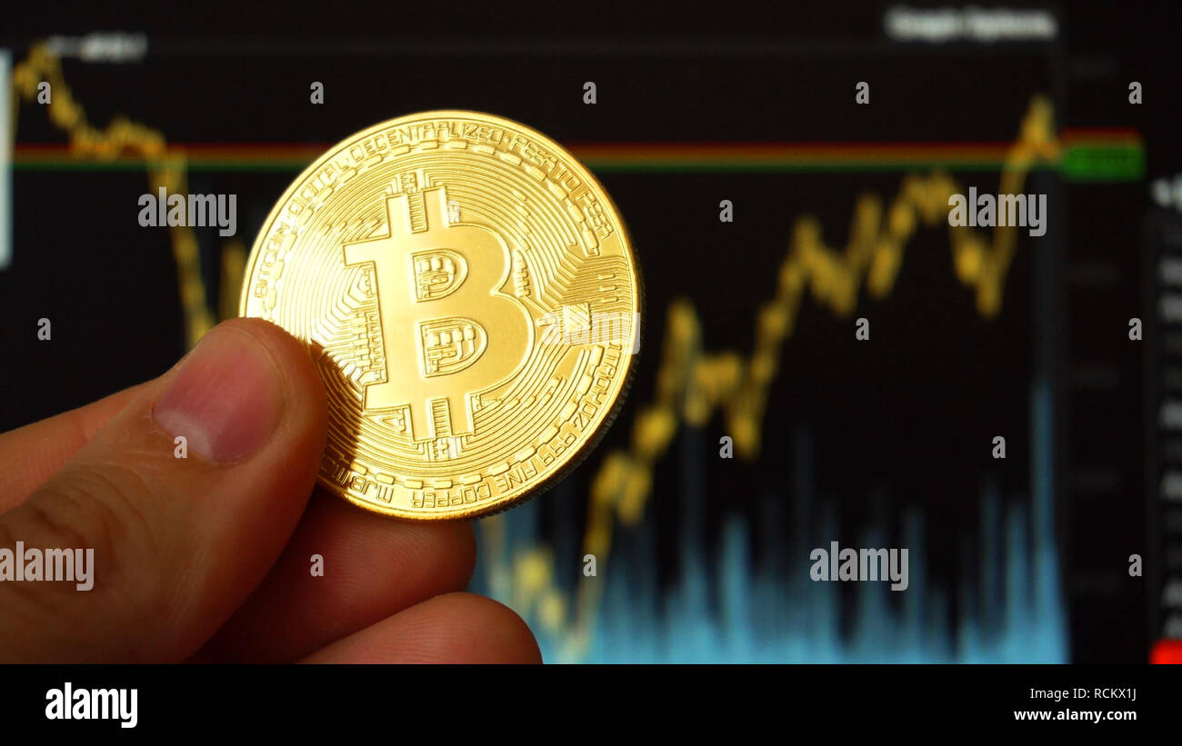 Hand holding digital BTC Bitcoin coin on front of charts Stock Photo