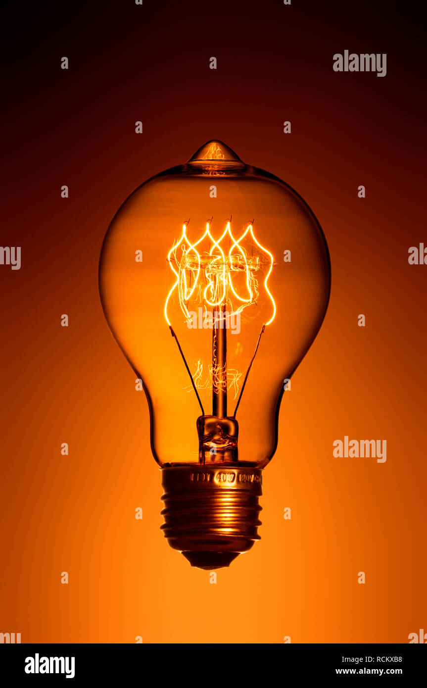 Illuminated retro light bulb with screw fitting, close up, orange colour background Stock Photo