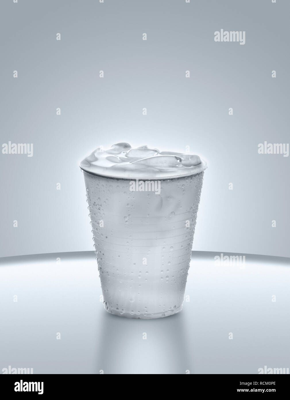 Disposable plastic cup full of water and ice, grey background, close up Stock Photo