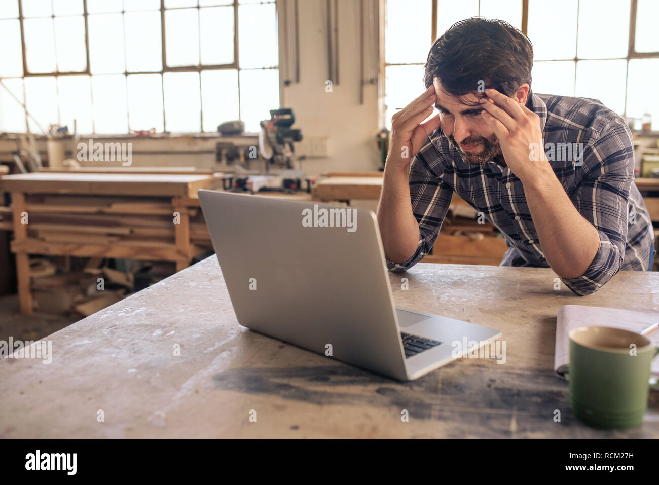 Stressed out woodworker using a laptop in his carpentry studio Stock Photo