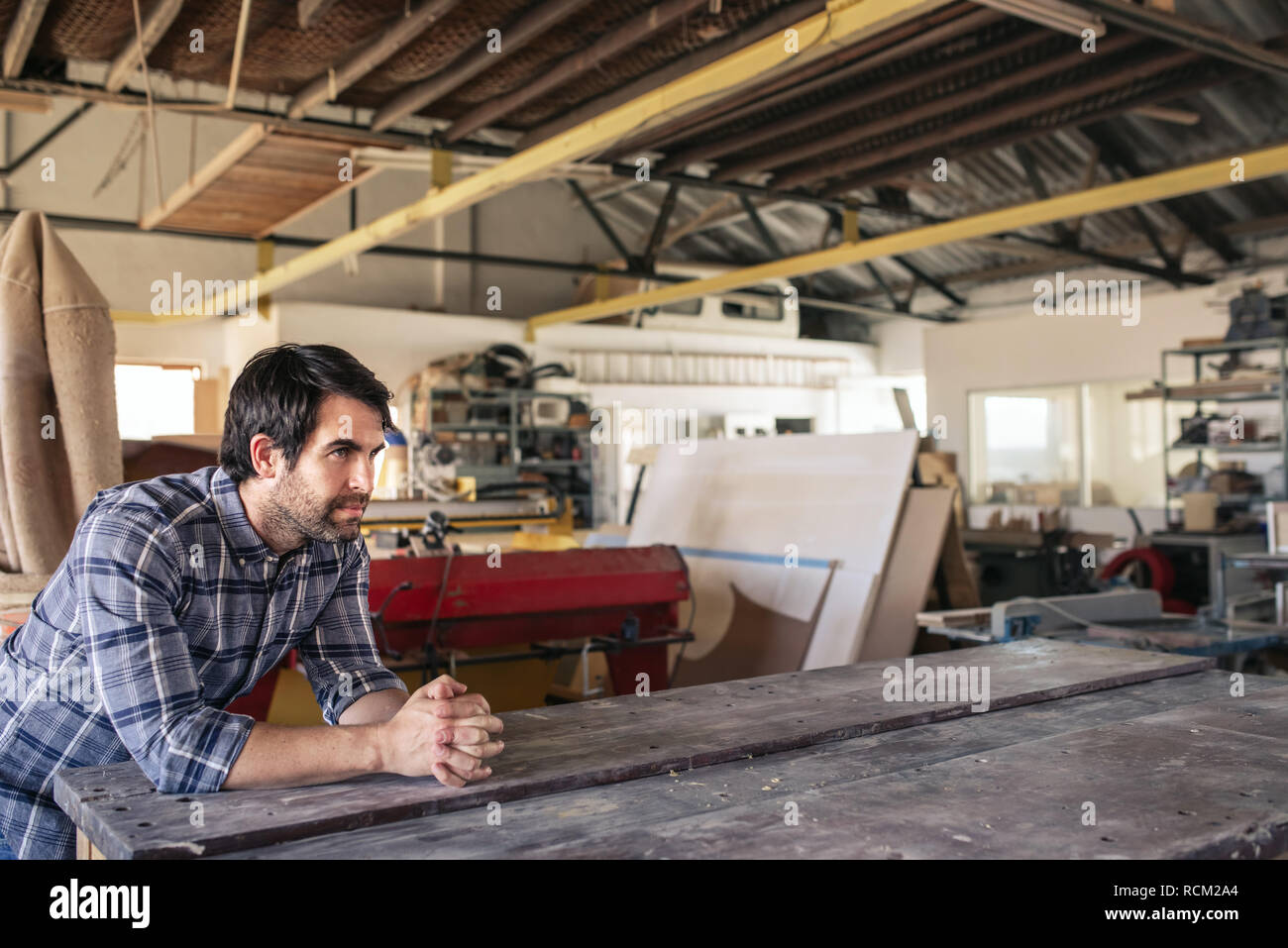 Woodworker leaning on a workshop bench deep in thought Stock Photo