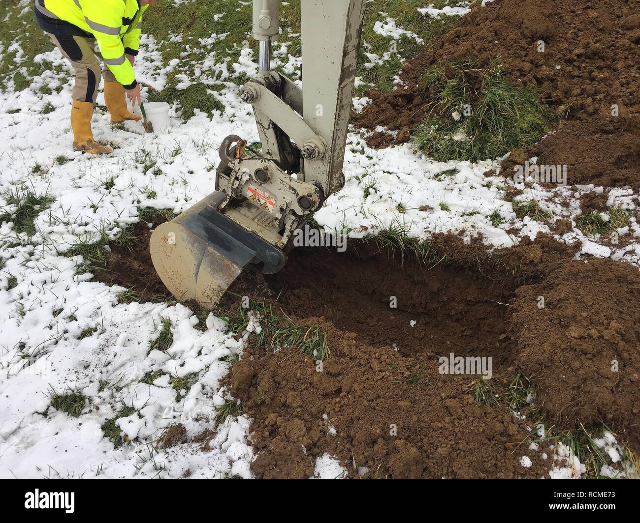 Excavator shovel digs into a ground covered with snow. Stock Photo