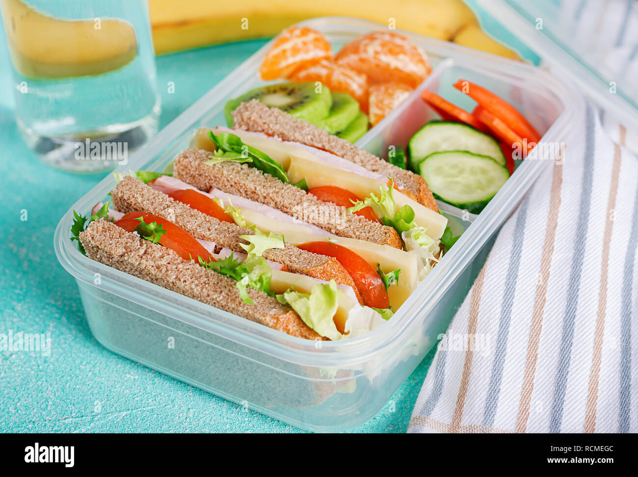 School lunch box with sandwich, vegetables, water, and fruits on