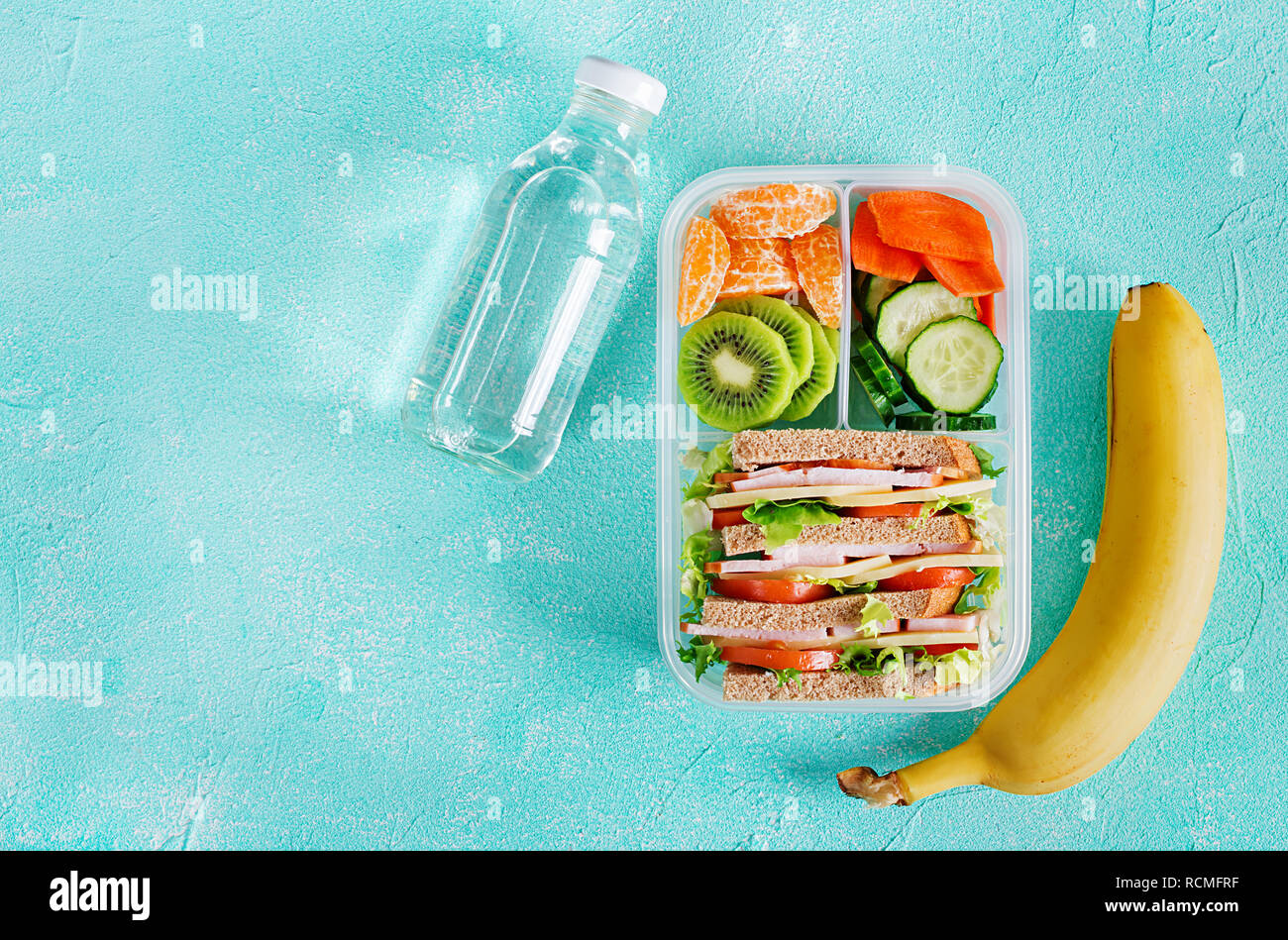 School lunch box with sandwich, vegetables, water, and fruits on table