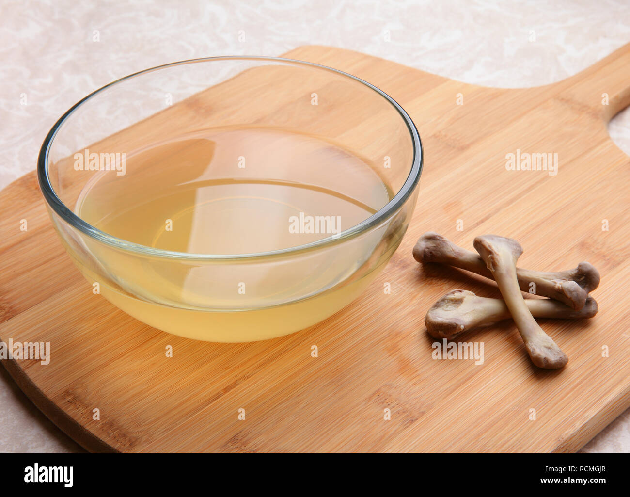 freshly made chicken bone broth in glass bowl with bones nearby Stock Photo