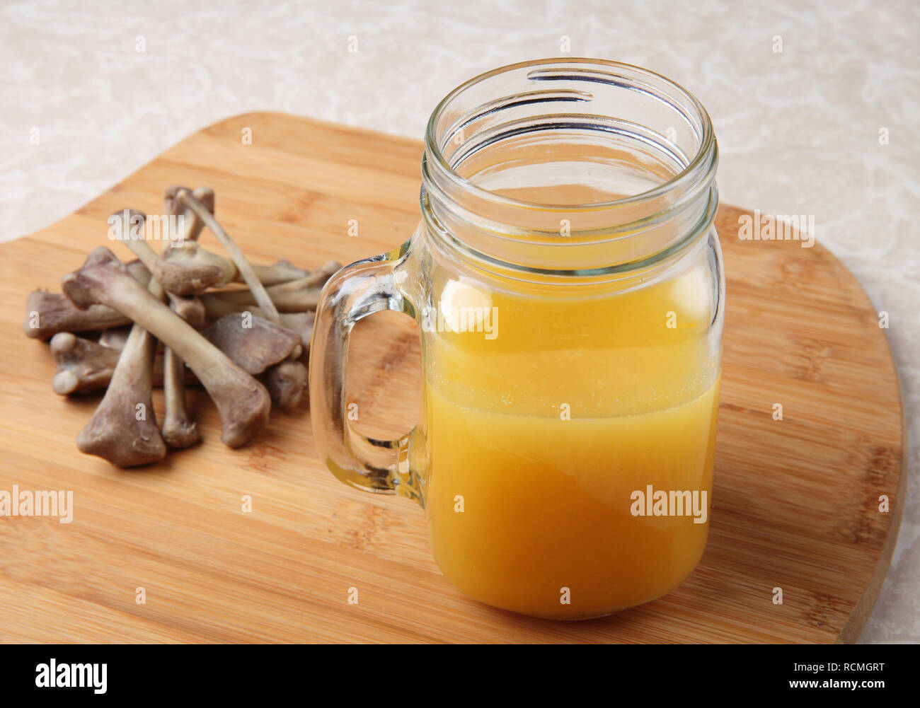 freshly made chicken bone broth in glass jar with bones nearby Stock Photo
