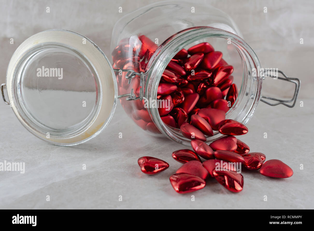Spilled jar of red hearts on its side.  Tan background. Stock Photo