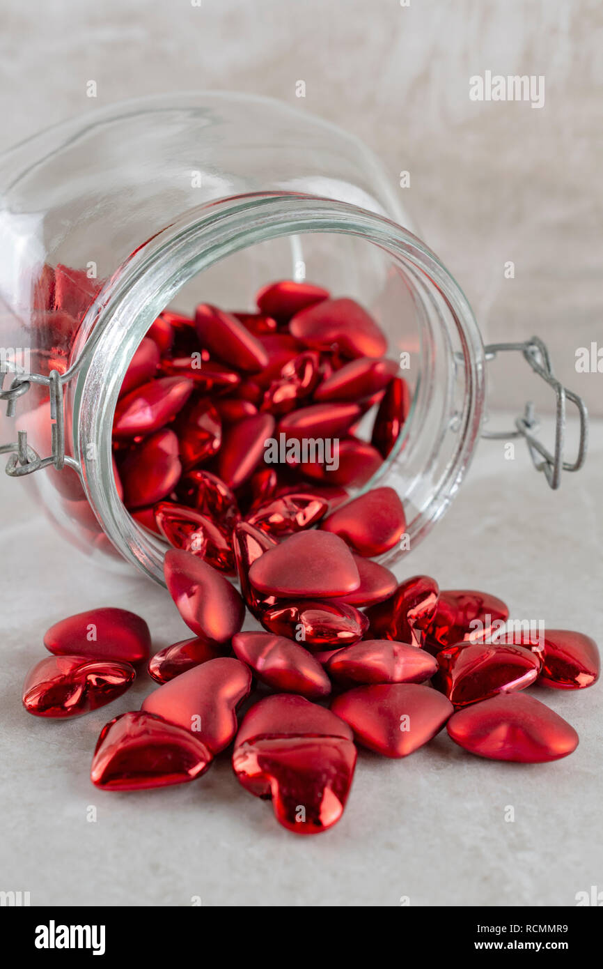 Jar of red hearts spilled onto its side.  Portrait view. Stock Photo