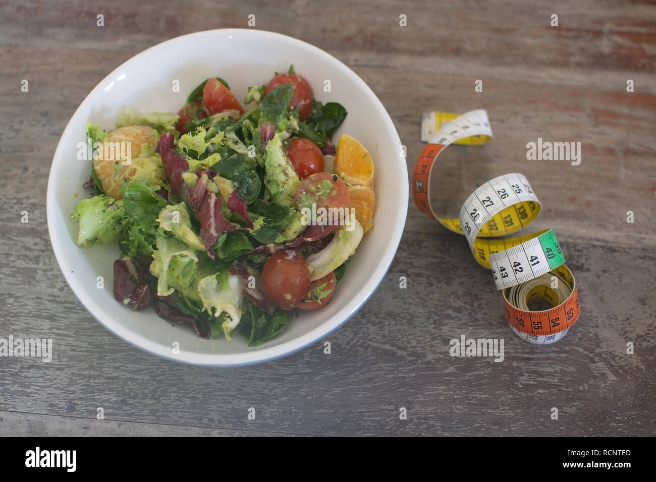 Mixed green and purple salad with measuring tape on shabby brown wooden table dieting fitness health conceptual background. Stock Photo