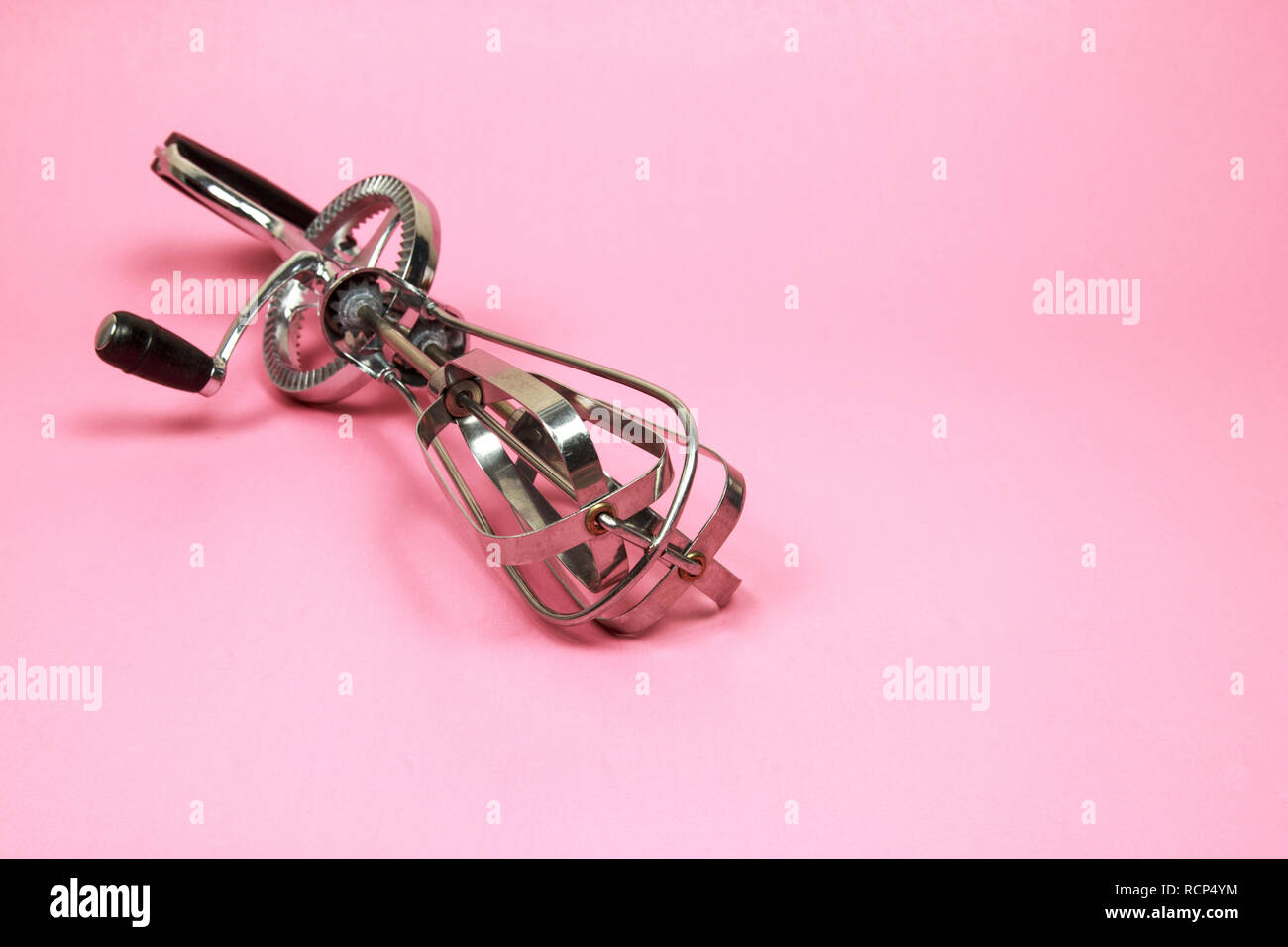 Stainless steel manual hand crank egg beaters on pink pastel background
