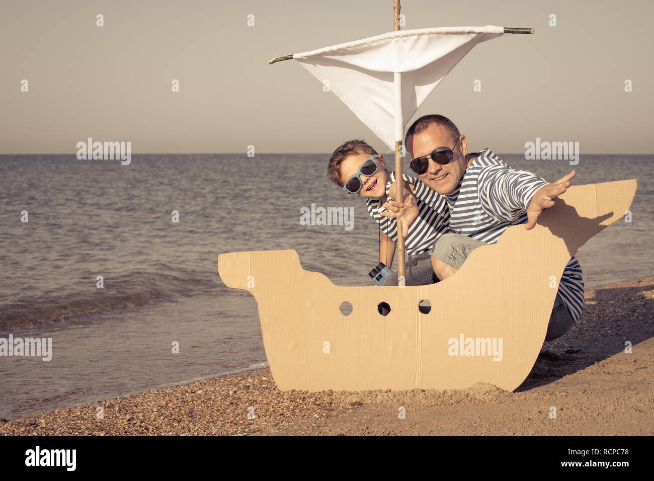 Father and son playing on the beach at the day time. They are dressed in sailor's vests. Concept of sailors on vacation and friendly family. Stock Photo