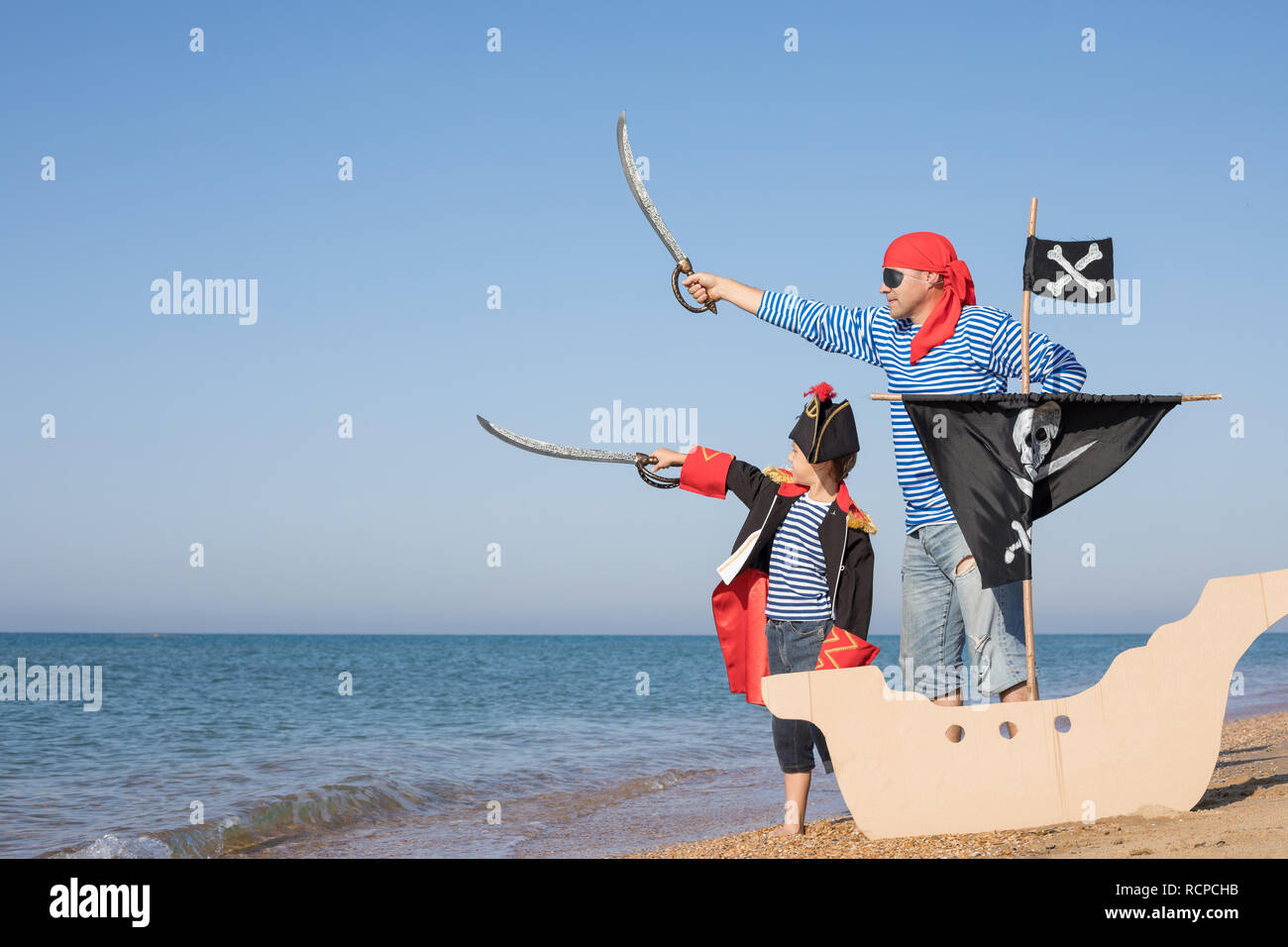 Father and son playing on the beach at the day time. They are dressed in sailor's vests and pirate costumes. Concept of happy game on vacation and fri Stock Photo