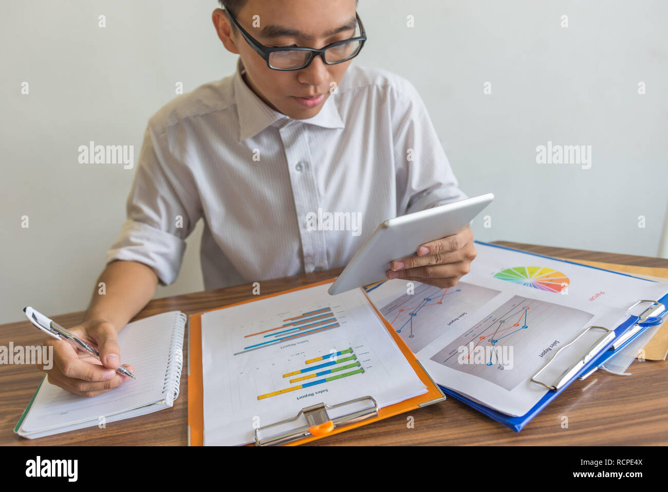 Man using tablet to check data and writing notes Stock Photo
