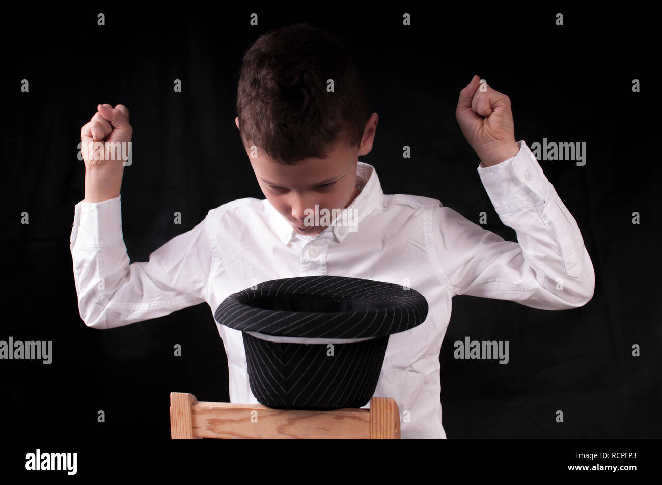 Boy in a white shirt against a black background conjures from a hat Stock Photo